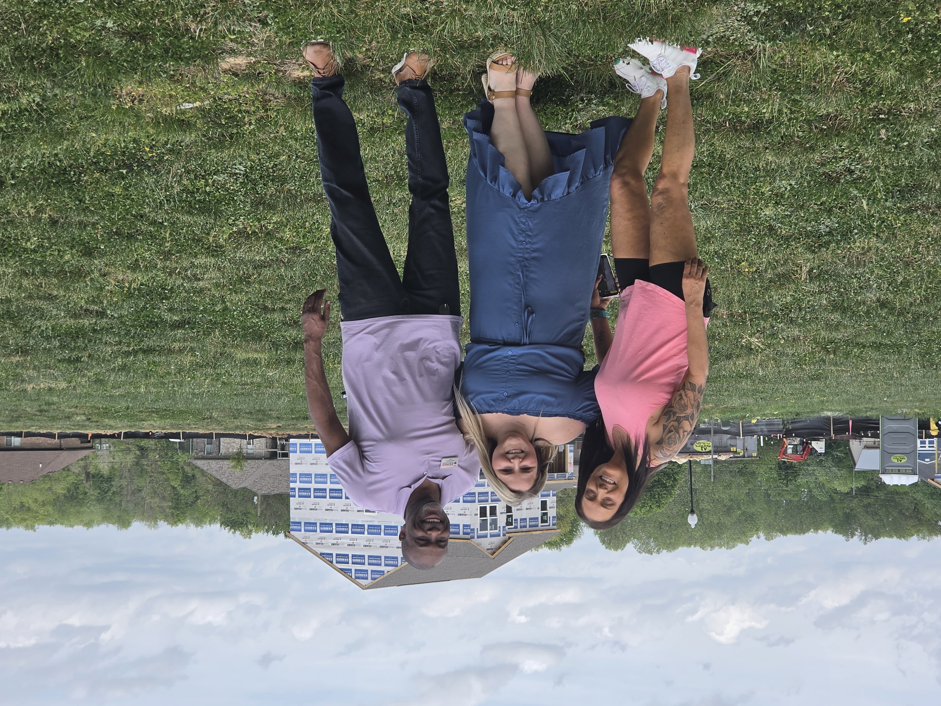 Three people standing in a grass field with a new construction home framed in the background.