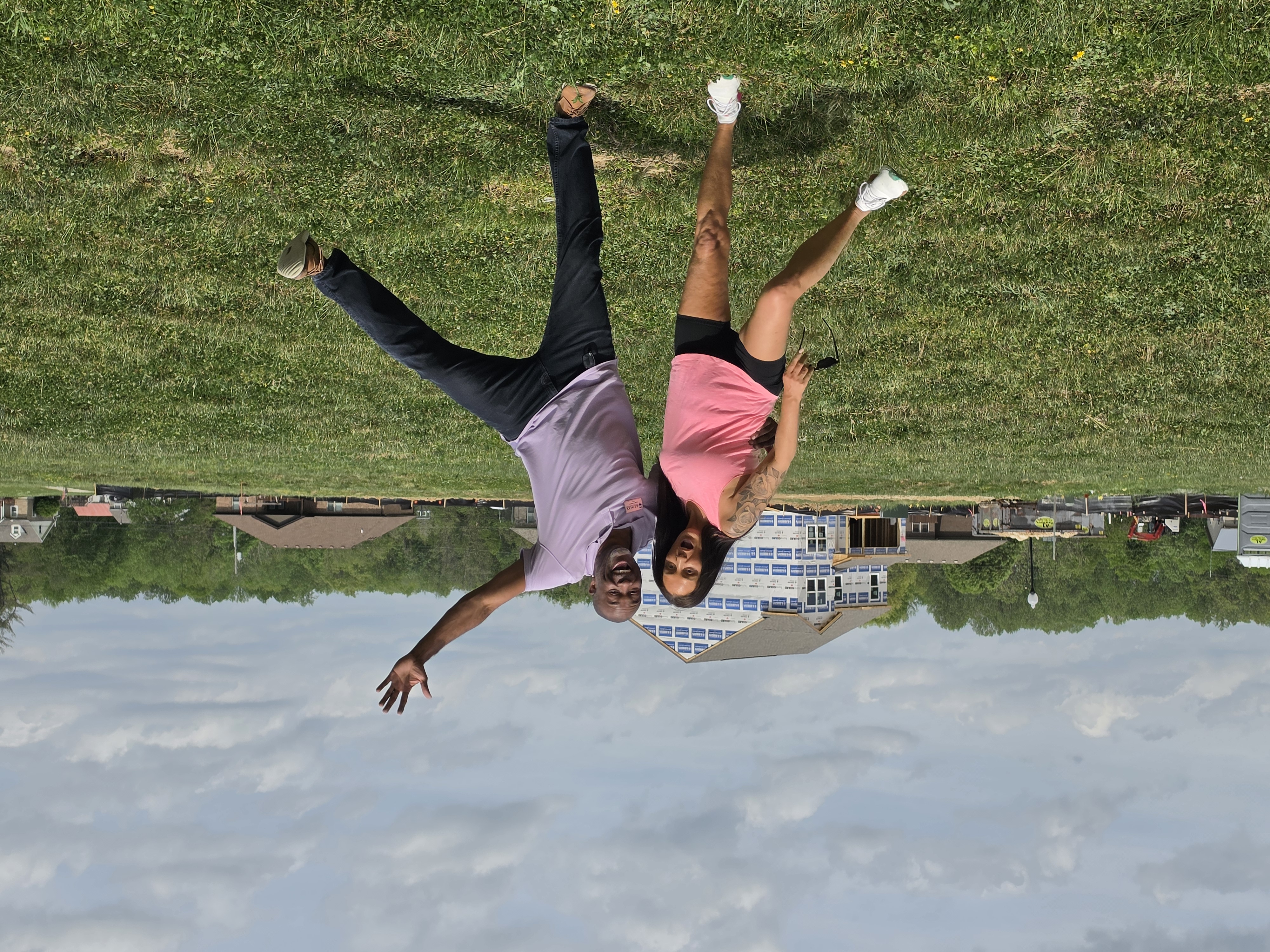 Two people posing playfully in a field in front of a home under construction.